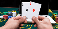Un jugador con dos ases en la mano en una mesa de Blackjack con fichas y un ordenador portátil.